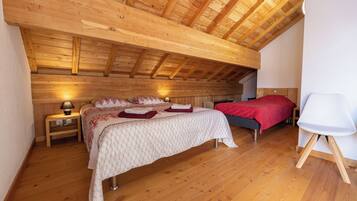 A bedroom with a sloped wooden ceiling, two beds, bedside tables with lamps, and a white chair.