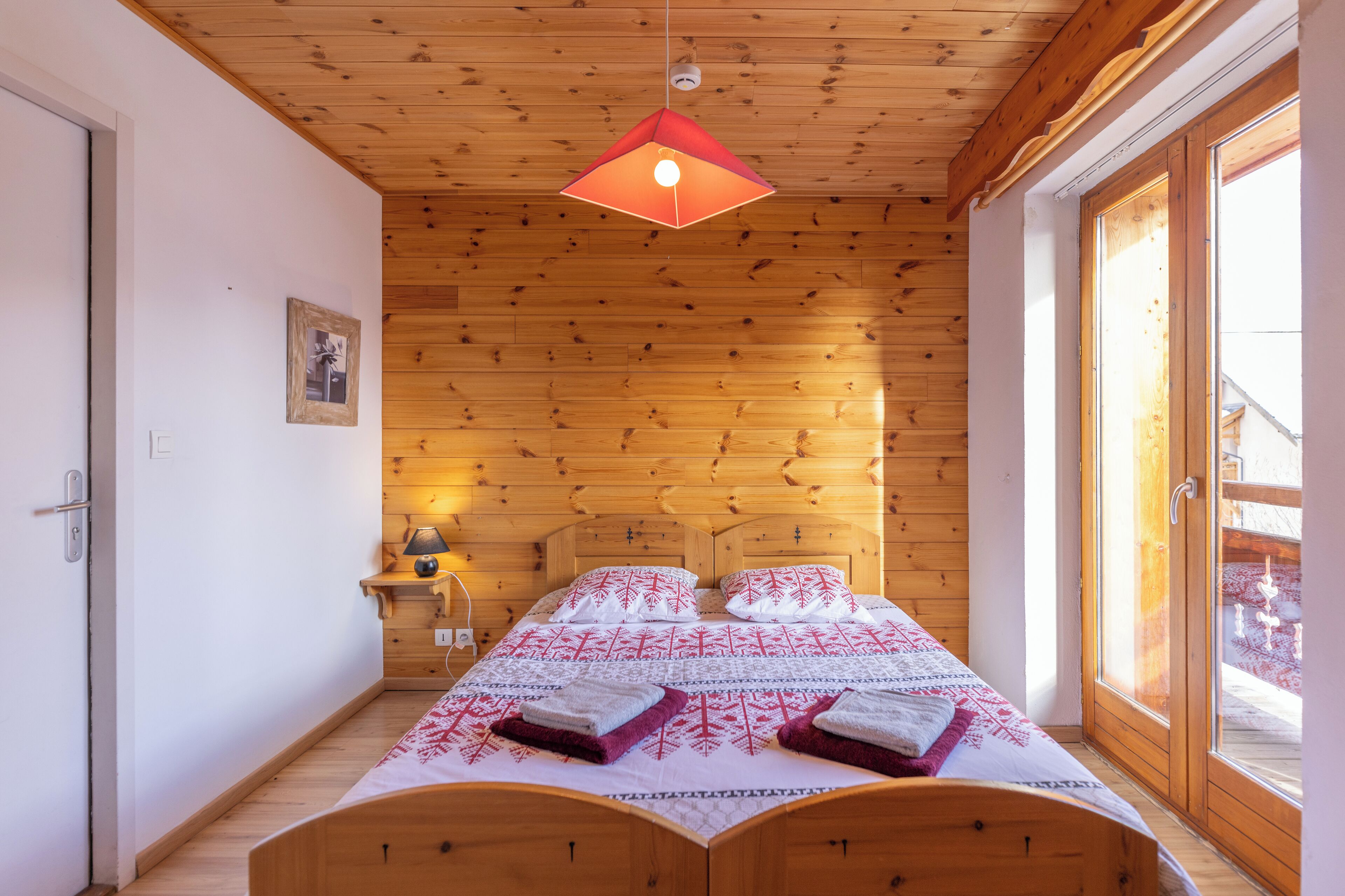 A wooden-paneled bedroom with a bed, a hanging light fixture, and a window with a view of a snowy landscape.