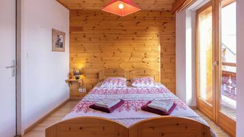 A wooden-paneled bedroom with a bed, a hanging light fixture, and a window with a view of a snowy landscape.