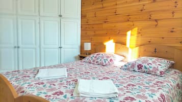 Une chambre aux murs lambrissés, avec un lit, une literie à motifs floraux et une table de chevet sur laquelle se trouve une lampe.