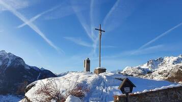 Paesaggio montano innevato con una croce di legno e un monumento in pietra.