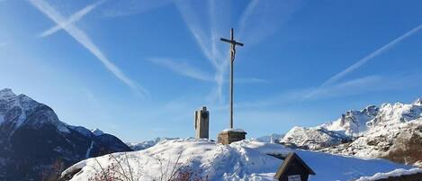 Paisaje nevado de una montaña con una cruz de madera y un monumento de piedra.