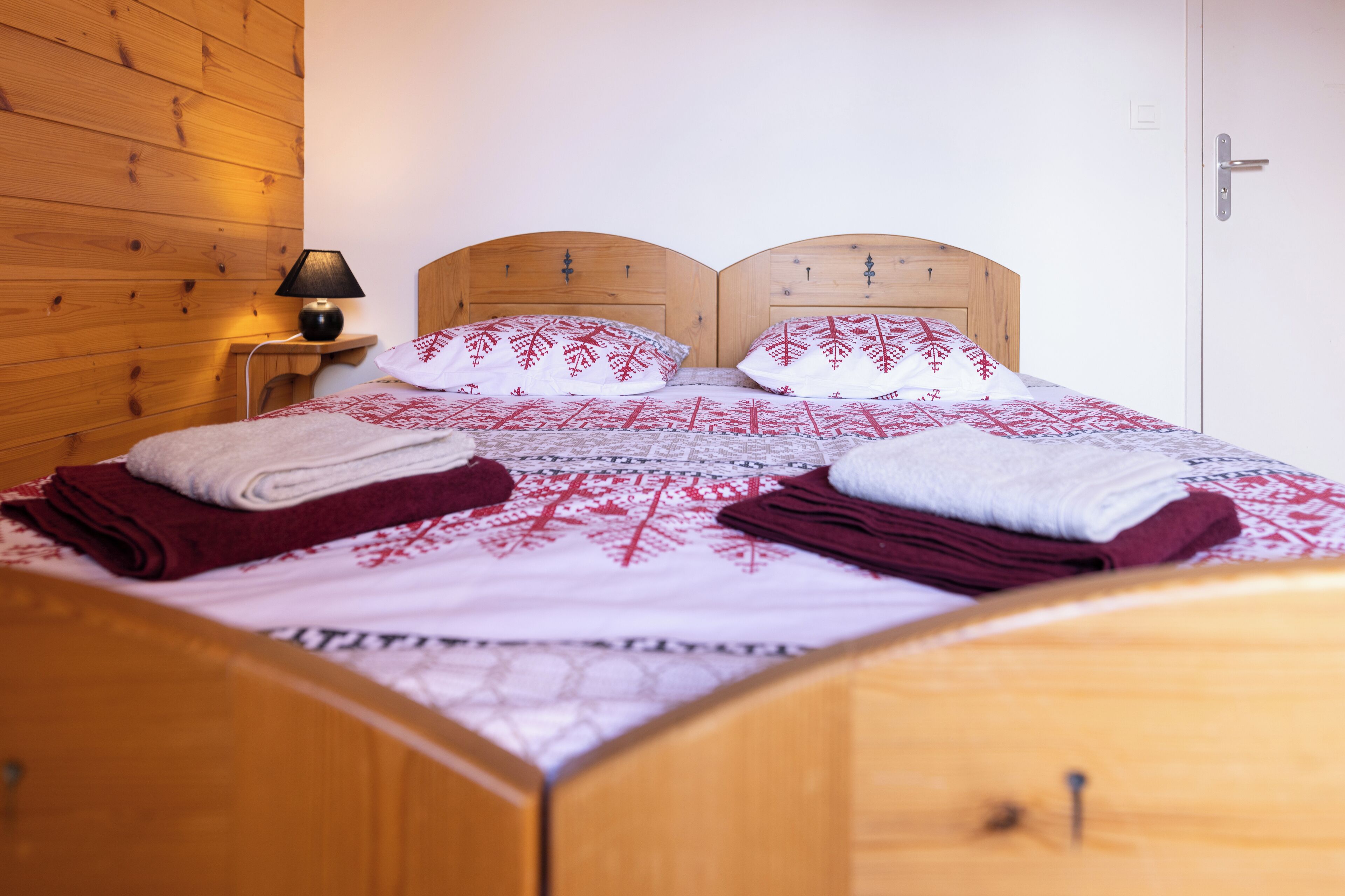 Una cama de madera con cabecera, una mesita de noche con lámpara y una puerta a la derecha.