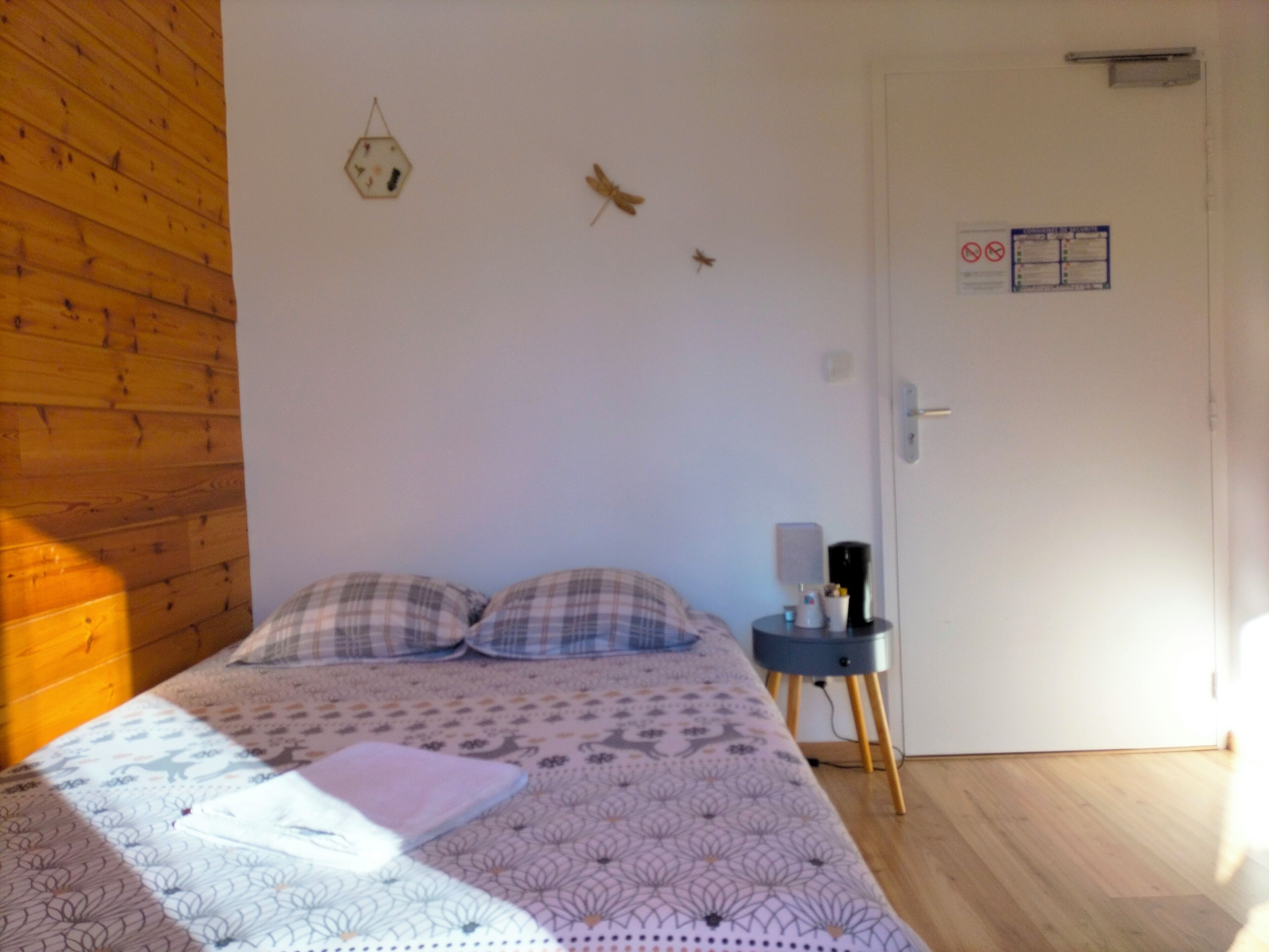 Un dormitorio con una cama, dos almohadas, una mesita de noche con lámpara y un reloj de pared.