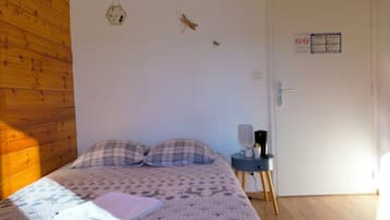 Un dormitorio con una cama, dos almohadas, una mesita de noche con lámpara y un reloj de pared.