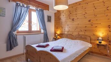 A bedroom with a wooden headboard, a bed with white bedding, two bedside lamps, a window with curtains, and a wooden wall paneling.