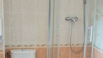 Une salle de bain avec des toilettes, une douche à parois de verre et des murs carrelés.