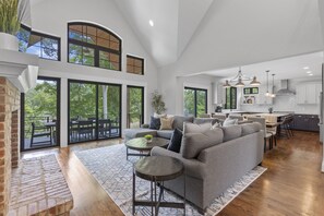 A spacious living area with a gray sectional sofa, a small round table, and a large window overlooking a patio. - Entertain, Enjoy Friends and Family - amazing amenities inc hot tub! (Catawba)