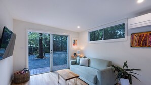 A modern living room with a sofa, a small table, a plant, and a TV on the wall. - Olive-Nature haven, outdoor bath, artistic cottage, 5 mins to Hyams Beach (Old Erowal Bay)