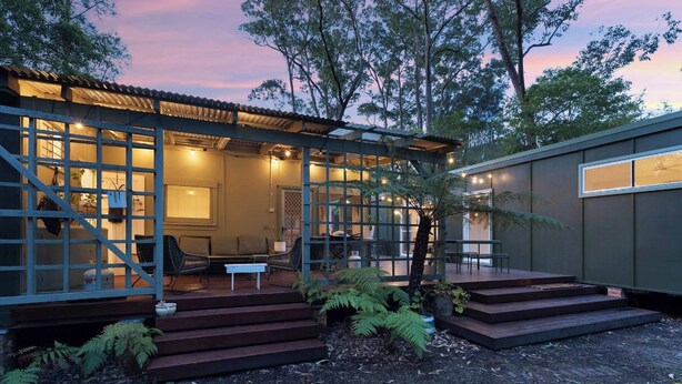 A modern house with a covered porch, steps leading to the entrance, and a garden area with ferns. - Olive-Nature haven, outdoor bath, artistic cottage, 5 mins to Hyams Beach (Old Erowal Bay)
