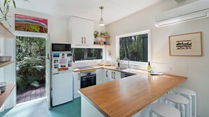 A modern kitchen with white cabinets, a wooden countertop, and a built-in oven. There is a window providing natural light and a view of greenery outside. - Olive-Nature haven, outdoor bath, artistic cottage, 5 mins to Hyams Beach (Old Erowal Bay)