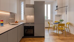 Moderni keittiö, jossa on sisäänrakennettu uuni, pesuallas ja ikkuna. Keittiössä on myös ruokailutila, jossa on keltaiset tuolit ja pöytä.