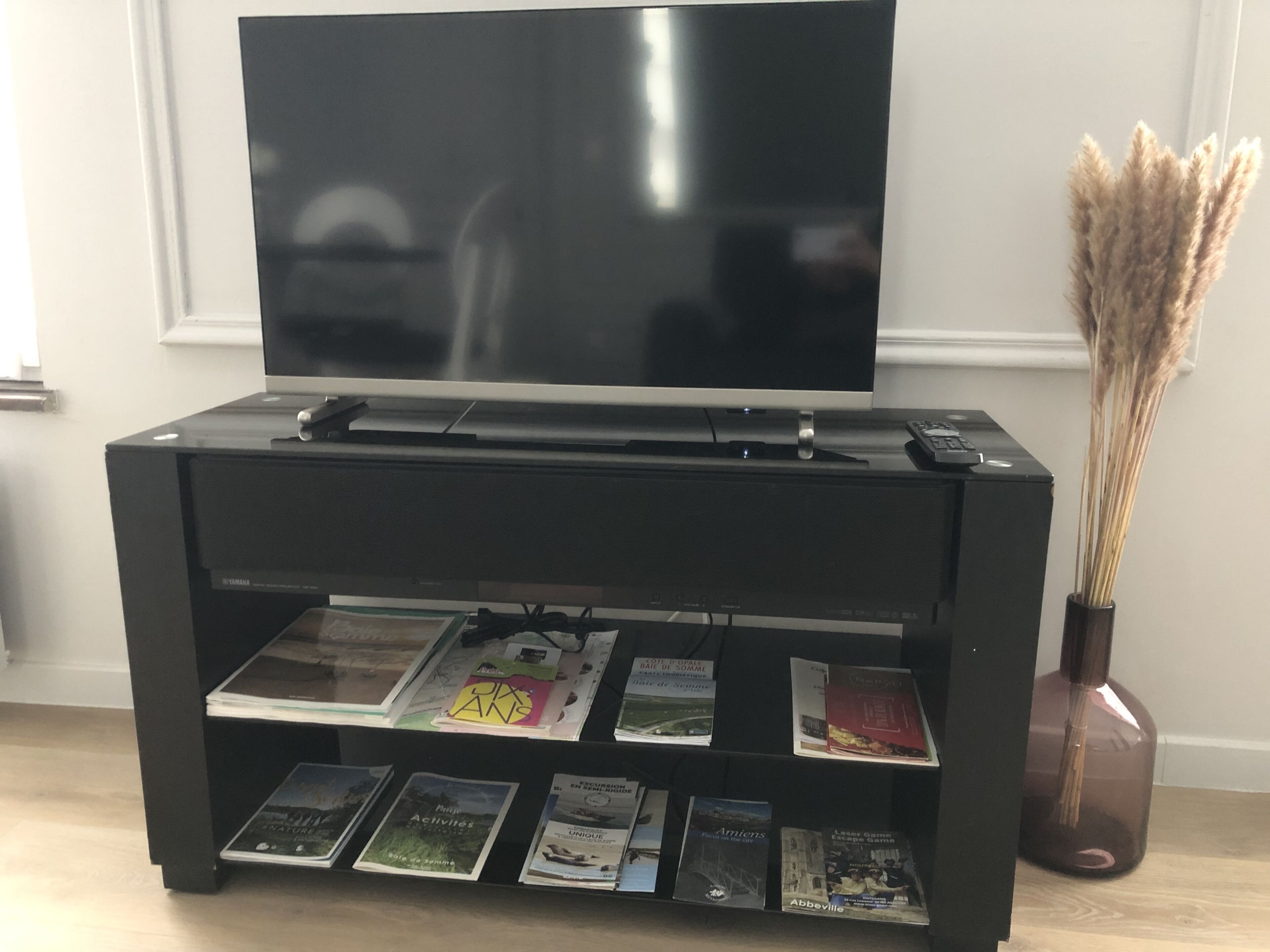 Eine schwarze Unterhaltungsanlage mit einem Flachbildfernseher obenauf und einem darunterliegenden Regal für verschiedene Zeitschriften und Bücher.