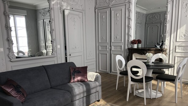 A living room with a grey sofa, white chairs, a dining table, and a clear glass coffee table.