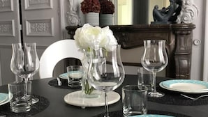 A dining table set with clear glassware and plates, a vase with white flowers, and a decorative statue.