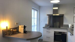 A modern kitchen with a built-in oven, a stainless steel range hood, and a countertop with a coffee machine. - Maison Gabriel Appartement Bulle (Abbeville)