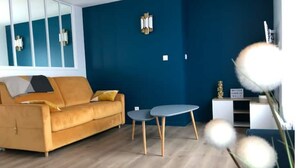 A modern living room with a sofa, a small table, and a decorative plant. - Maison Gabriel Appartement Bulle (Abbeville)