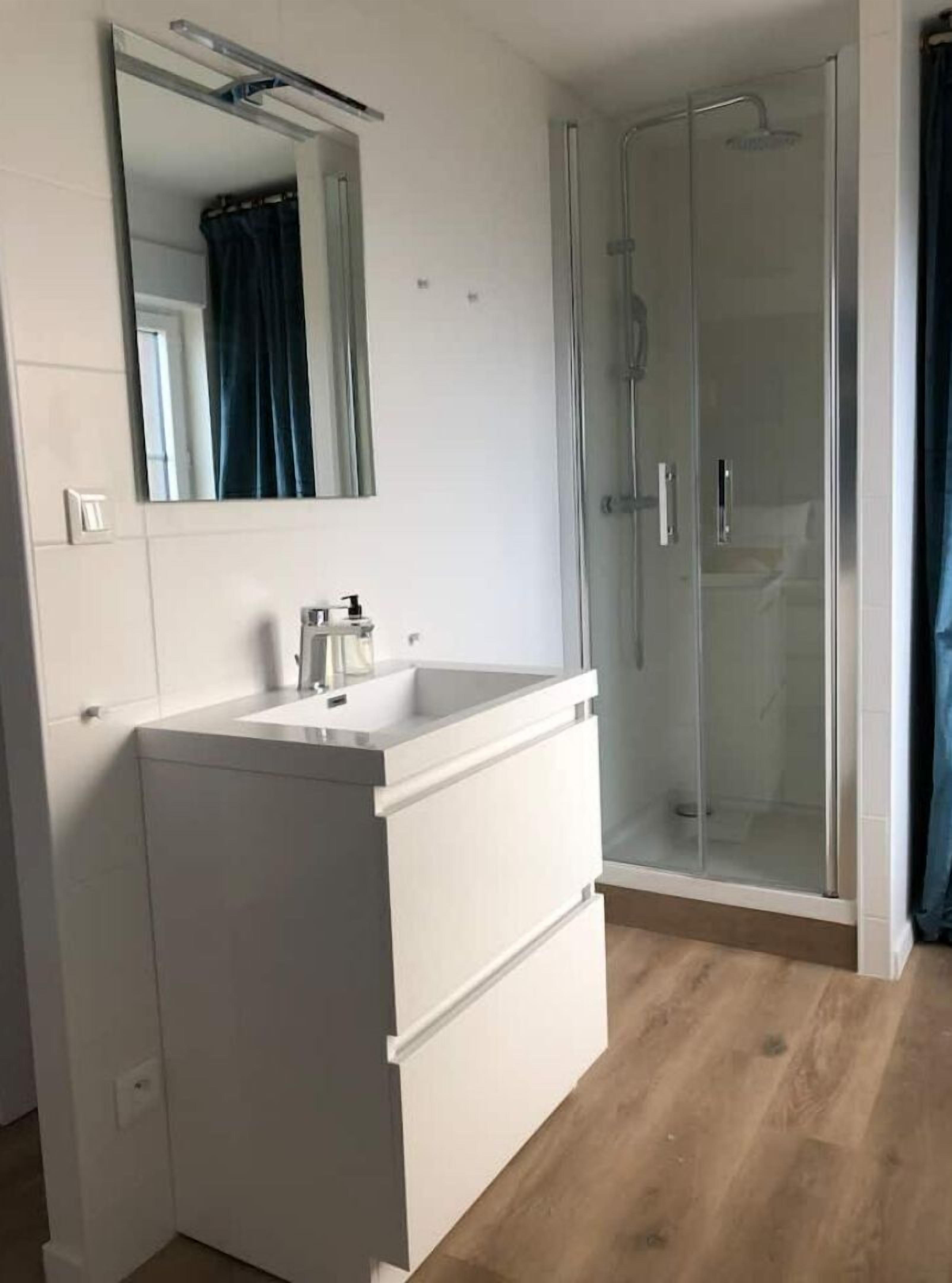 Ein Badezimmer mit weißem Waschtisch, einem Spiegel und einer Duschkabine aus Glas.