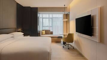 A modern hotel room with a large bed, a desk, a chair, and a TV mounted on the wall.