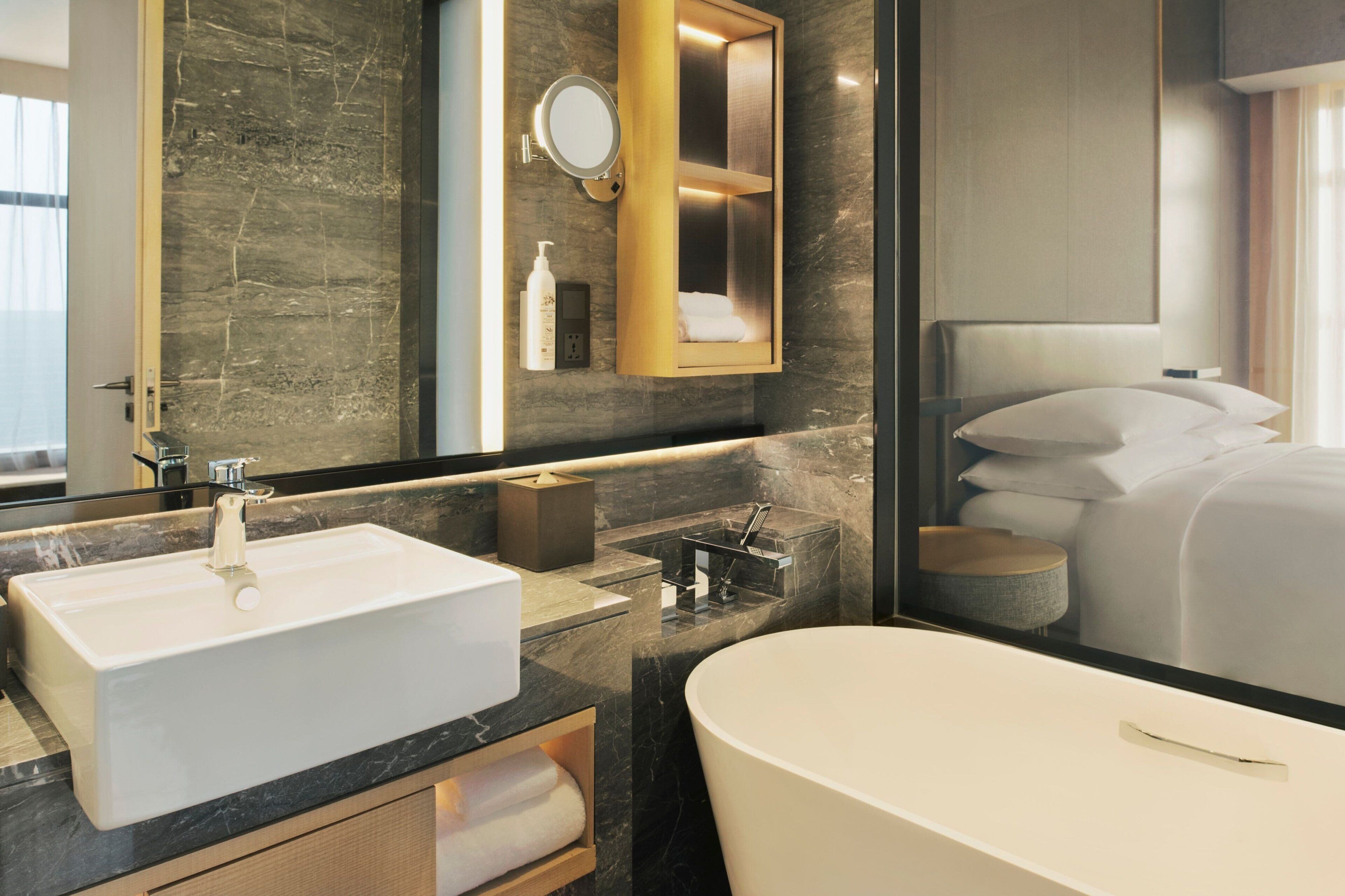 A modern bathroom with a large sink, a bathtub, a mirror, and a shelf with toiletries.