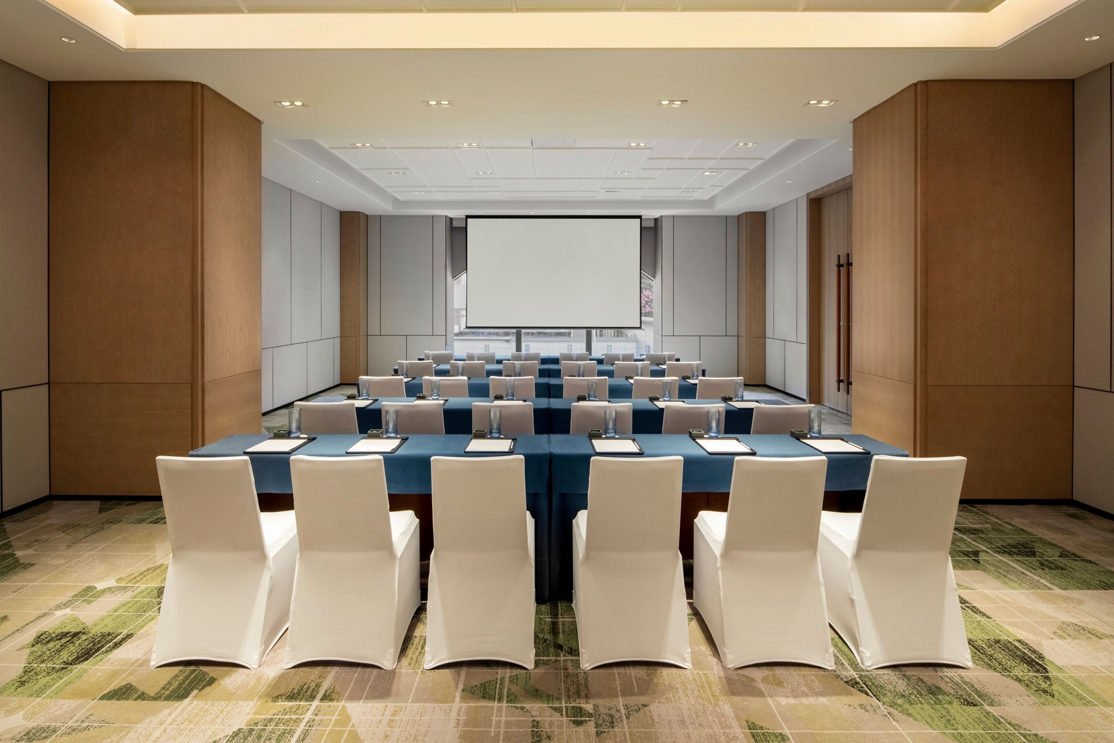 A conference room with a long table, white chairs, and a projector screen.