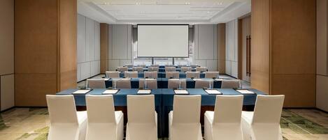 A conference room with a long table, white chairs, and a projector screen.