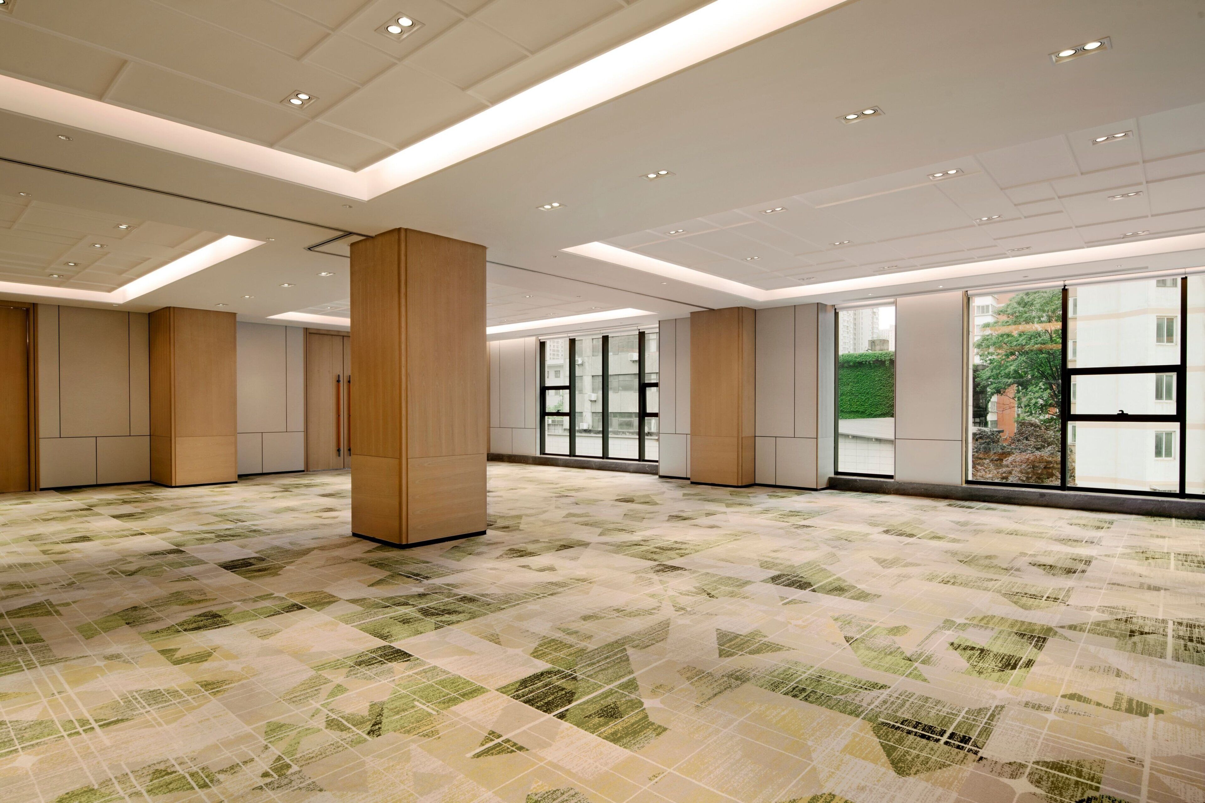 A spacious, modern hotel lobby with a geometric patterned floor, large windows offering views of greenery, and a clean, minimalist design.