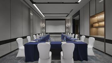 A conference room with a long table, white chairs, and a projector screen.