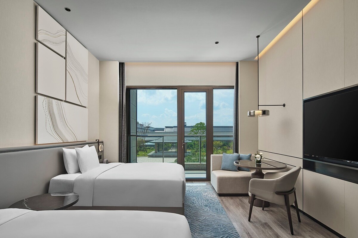 Habitación de hotel moderna con dos camas, un escritorio, un televisor y un balcón con vistas.