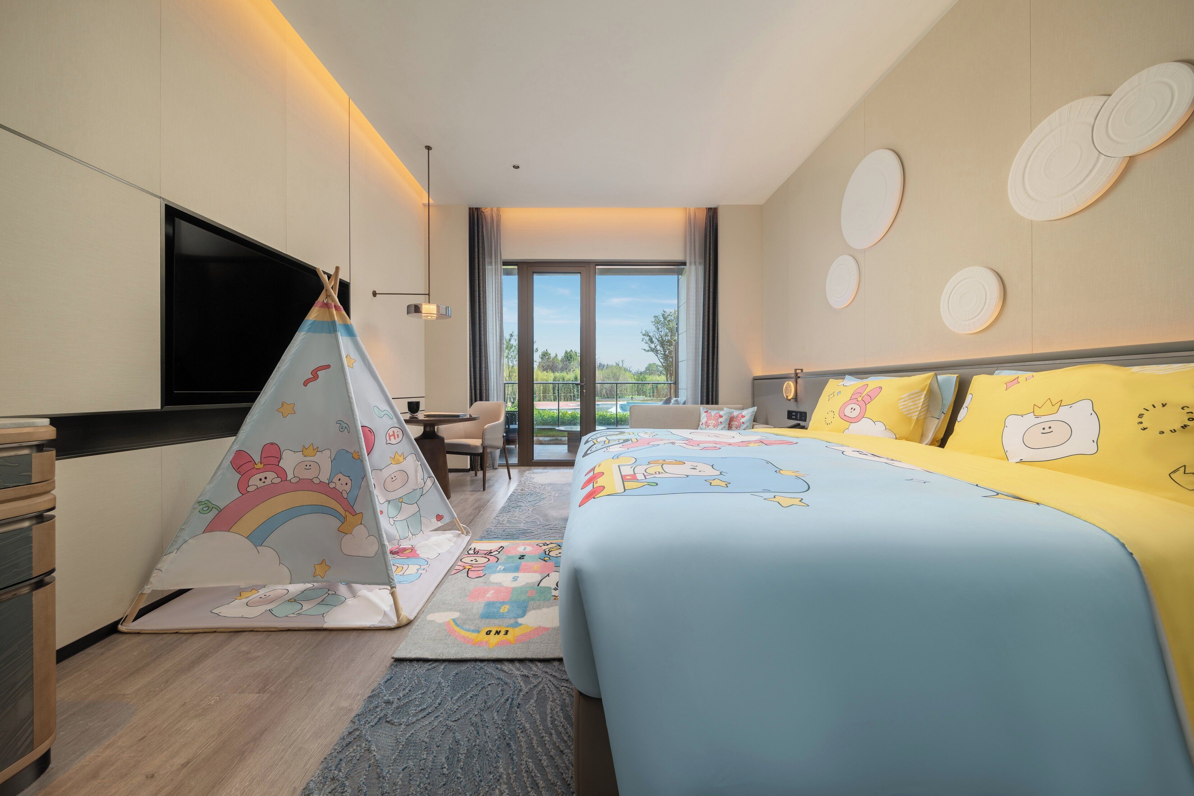 Habitación de hotel con cama, escritorio, silla, televisor y vistas al exterior.