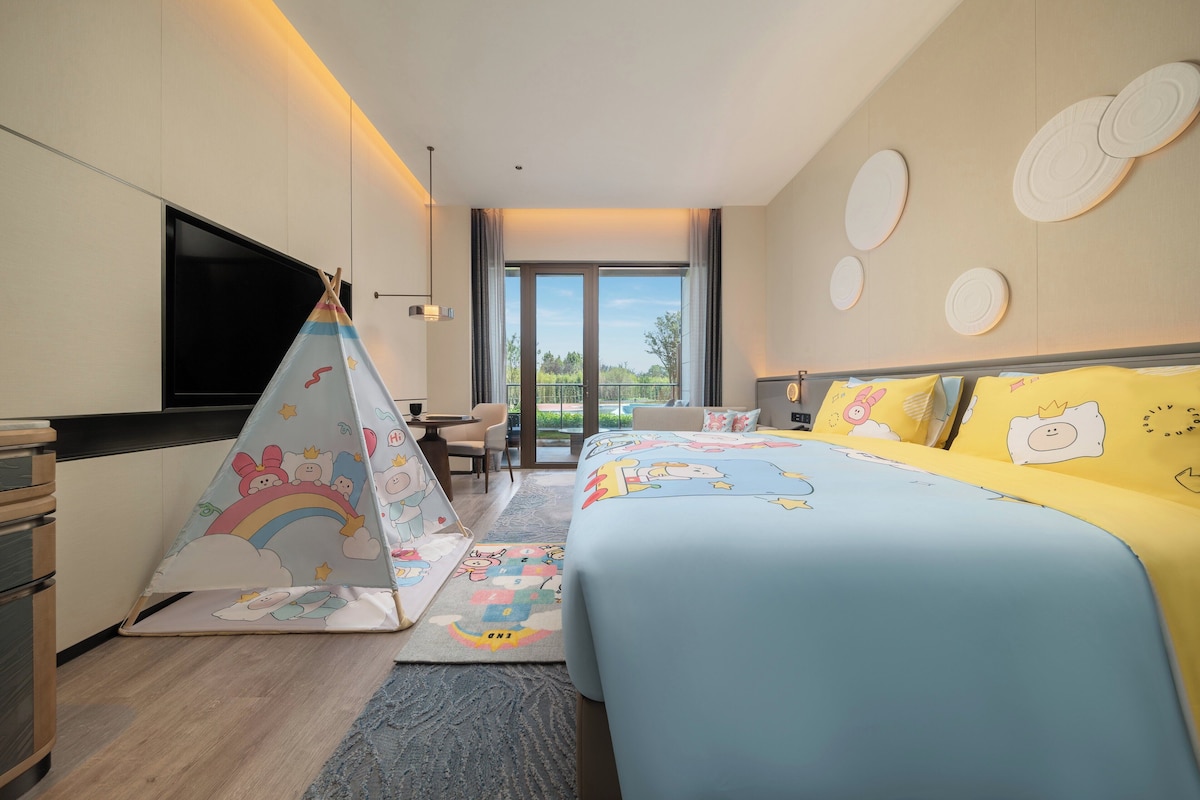 Habitación de hotel con cama, escritorio, silla, televisor y vistas al exterior.