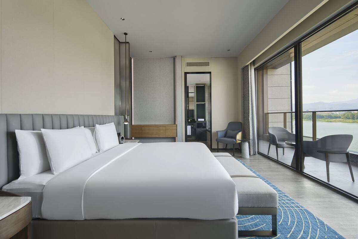 Ein modernes Hotelzimmer mit einem großen Bett, einer Sitzecke mit Stühlen und einem Balkon mit Blick.