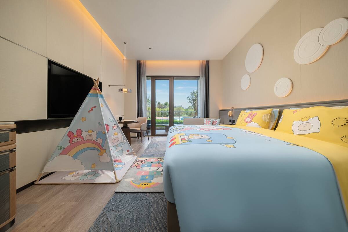 Ein Hotelzimmer mit Bett, Fernseher, Schreibtisch und Fenster mit Blick ins Freie.