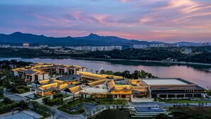 A modern hotel complex with multiple buildings, a landscaped garden, and a view of a river and mountains in the background. - Crowne Plaza Ganzhou by IHG (Ganzhou)