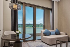 Una habitación moderna con una puerta de cristal que da a un balcón, una mesa redonda, un sofá con cojines y una lámpara colgante.
