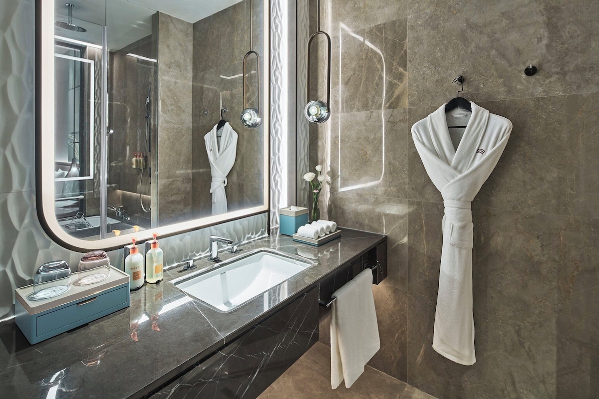 Un baño moderno con un espejo grande, un lavamanos y una bata colgada en un perchero.