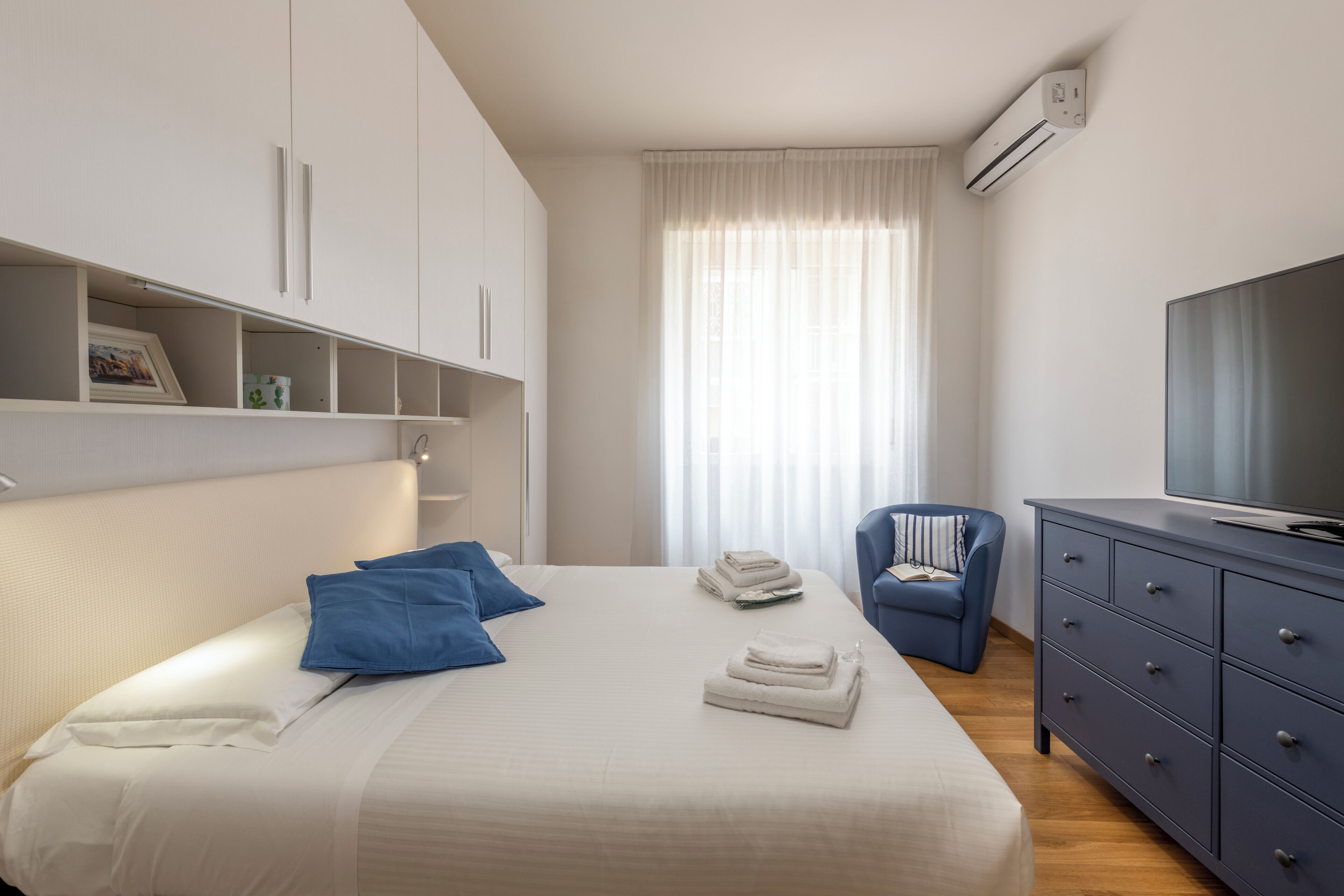 A hotel room with a bed, a TV, a chair, a dresser, and a window with curtains.