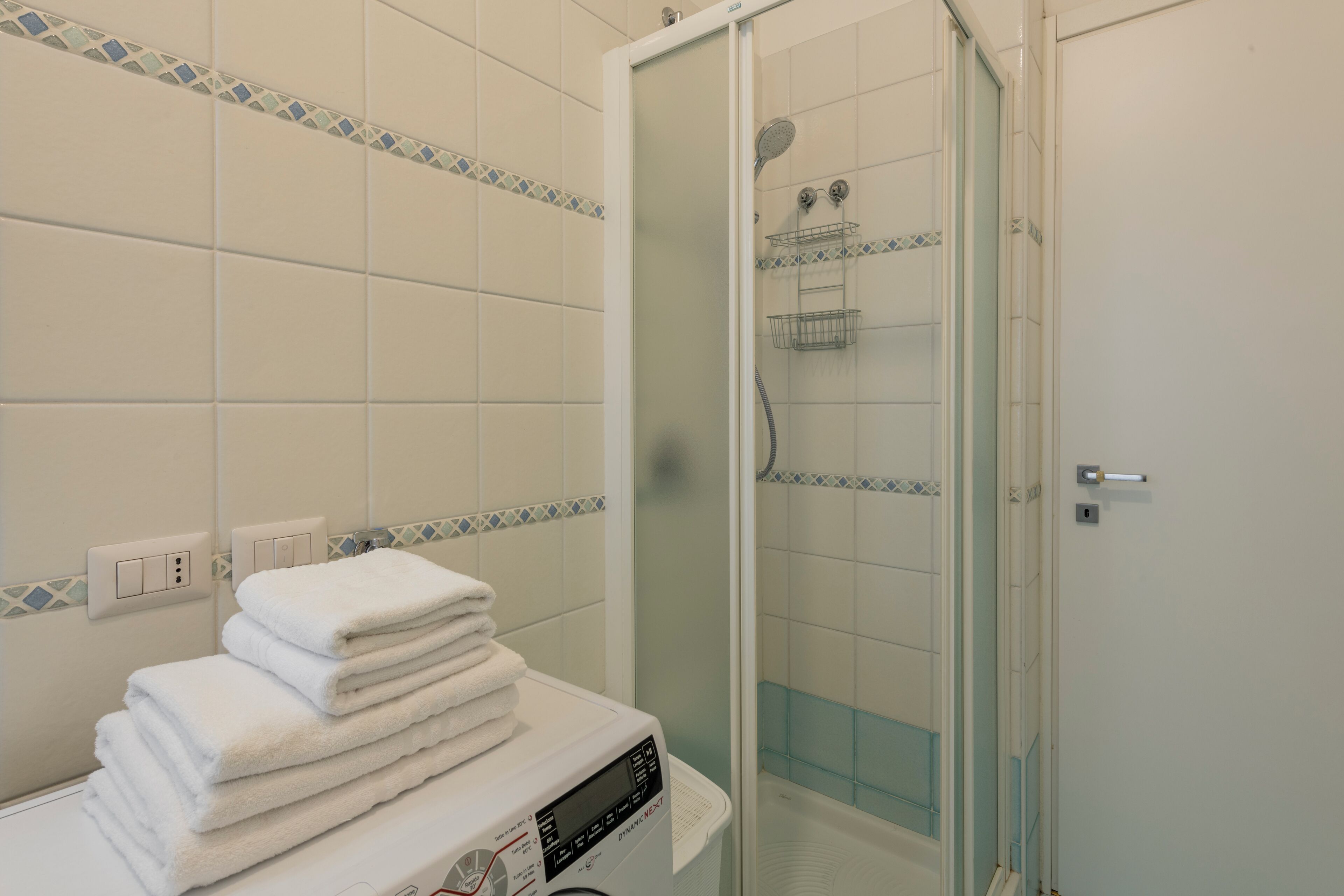 Une salle de bain avec une douche à parois de verre, une pile de serviettes blanches et un lave-linge.