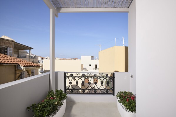 A balcony with a wrought iron railing, potted plants, and a view of neighboring buildings.