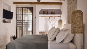 A bedroom with a bed, a television, a wooden ceiling, a macramé wall hanging, and a woven lamp. - Syroc Maison (Syros)