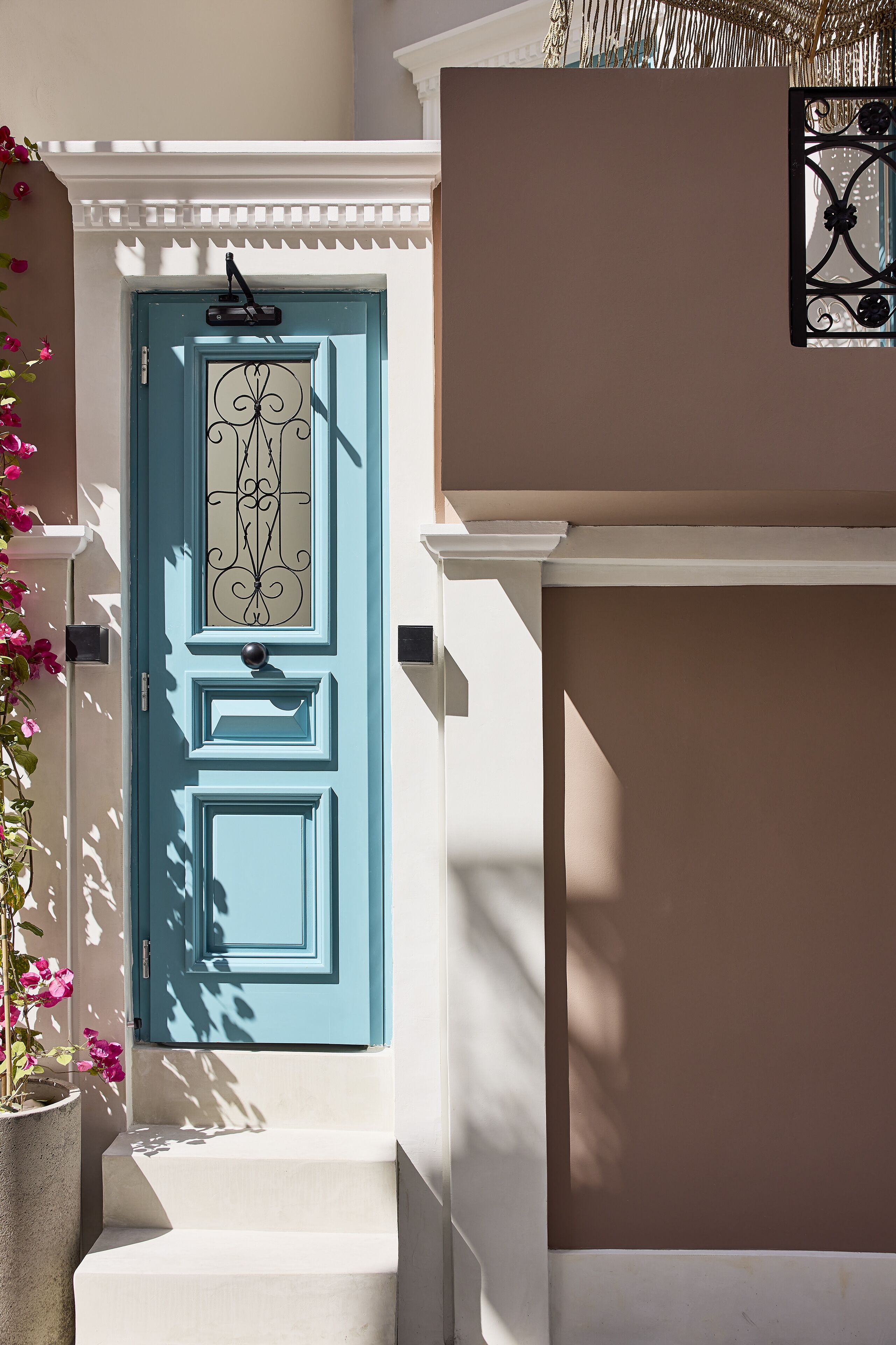 Una puerta azul con un panel de vidrio decorativo, unos escalones blancos que suben hacia ella y una planta en maceta a la izquierda.