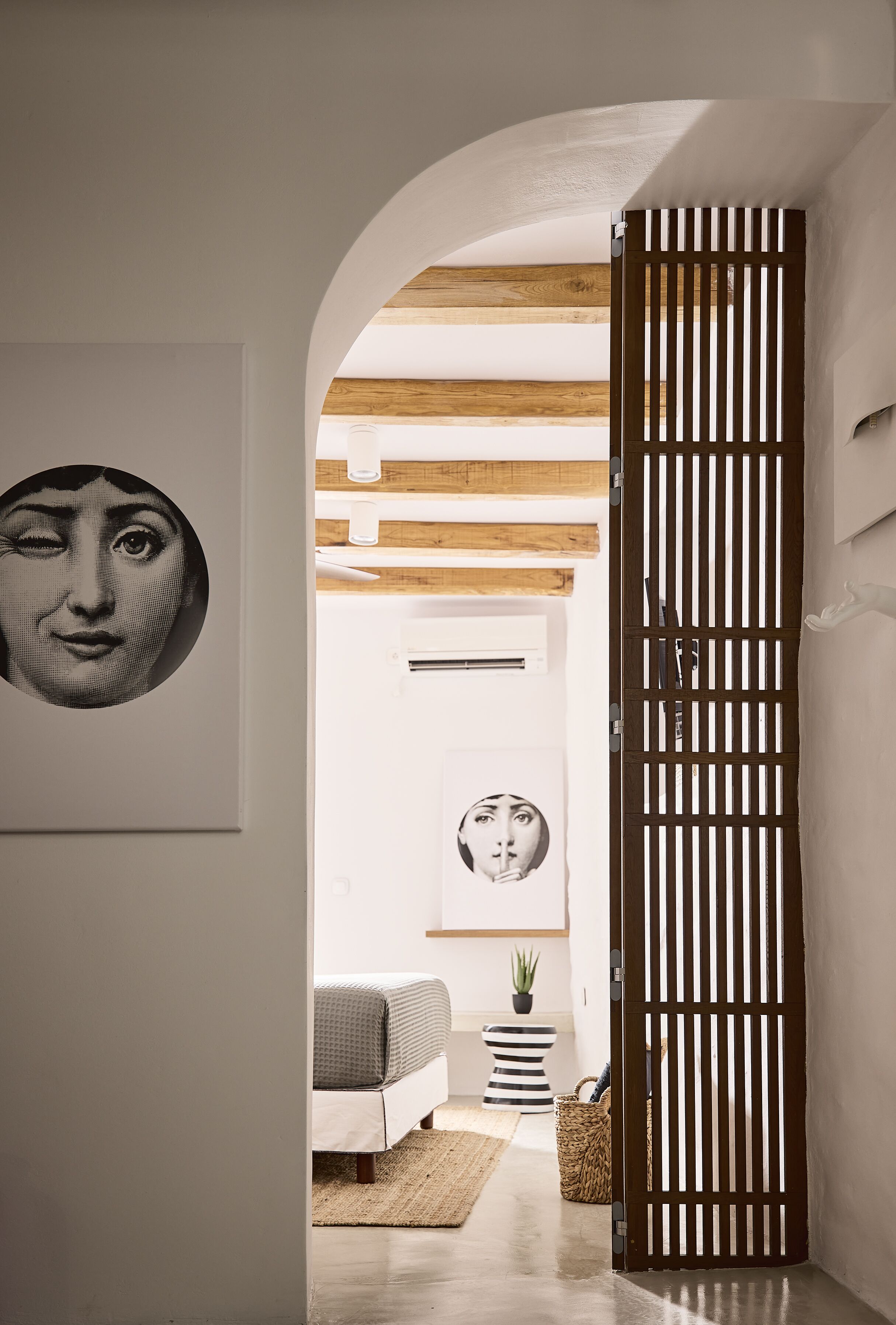 A hallway with a wooden door, a round wall art piece, a bed, and a small potted plant.