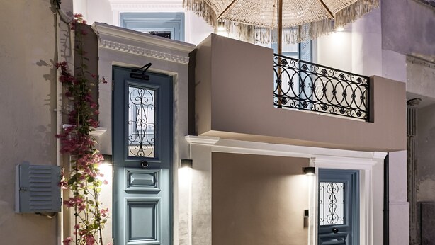 A multi-story building with a blue door, a balcony with a woven umbrella, and a staircase leading to the upper floor. - Syroc Maison (Syros)