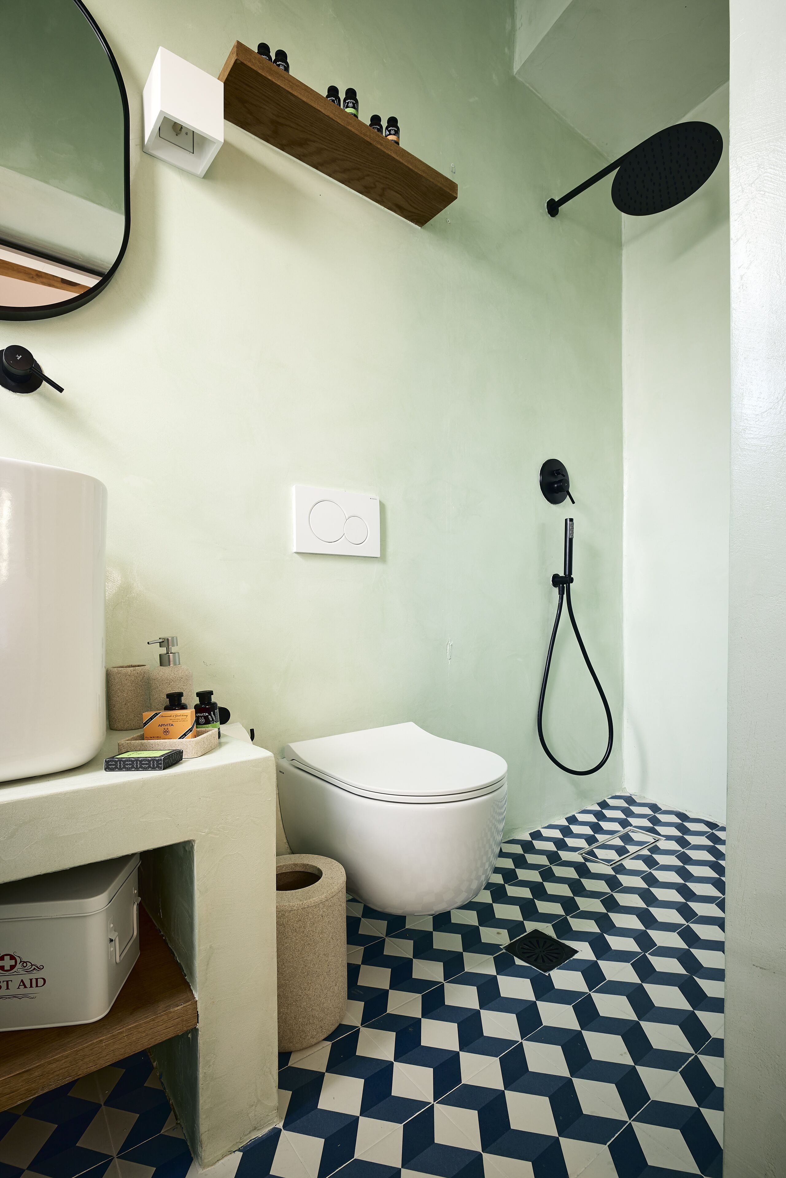 Un baño con inodoro, bidé y ducha. Hay un espejo, una estantería con artículos de aseo y un suelo estampado.