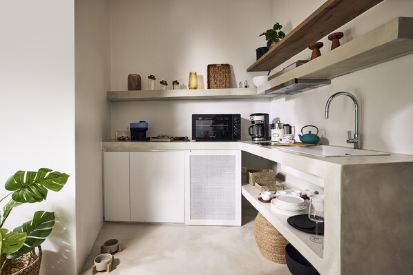 A compact kitchen with a built-in oven, coffee maker, and a sink. There are shelves above the counter holding various kitchen items.