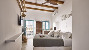 A bedroom with a bed, a ceiling fan, a wall-mounted air conditioner, and a view of the outside balcony. - Syroc Maison (Syros)