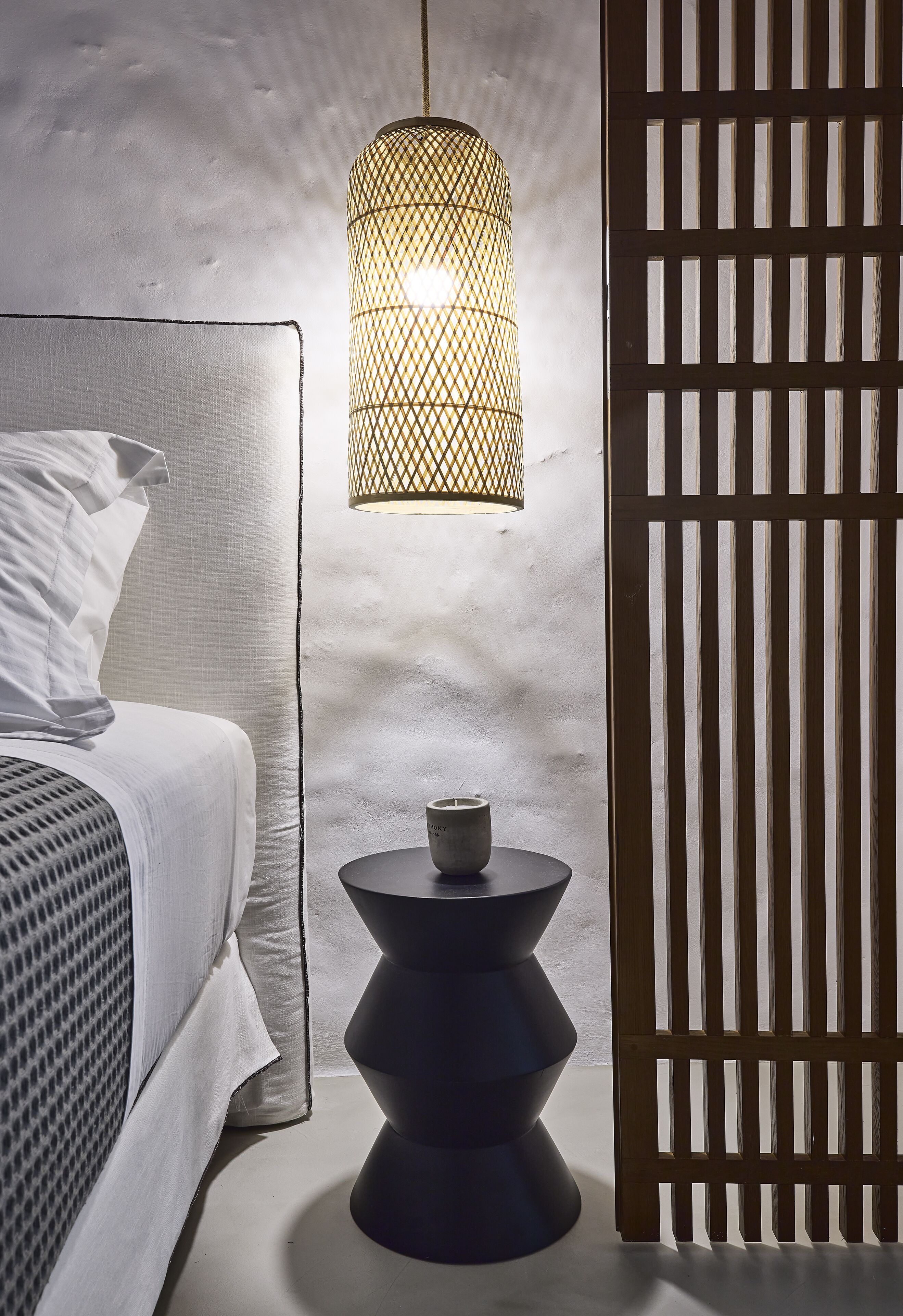 Een slaapkamer met een bed, een nachtkastje met een kopje, een hanglamp en een houten scheidingswand.