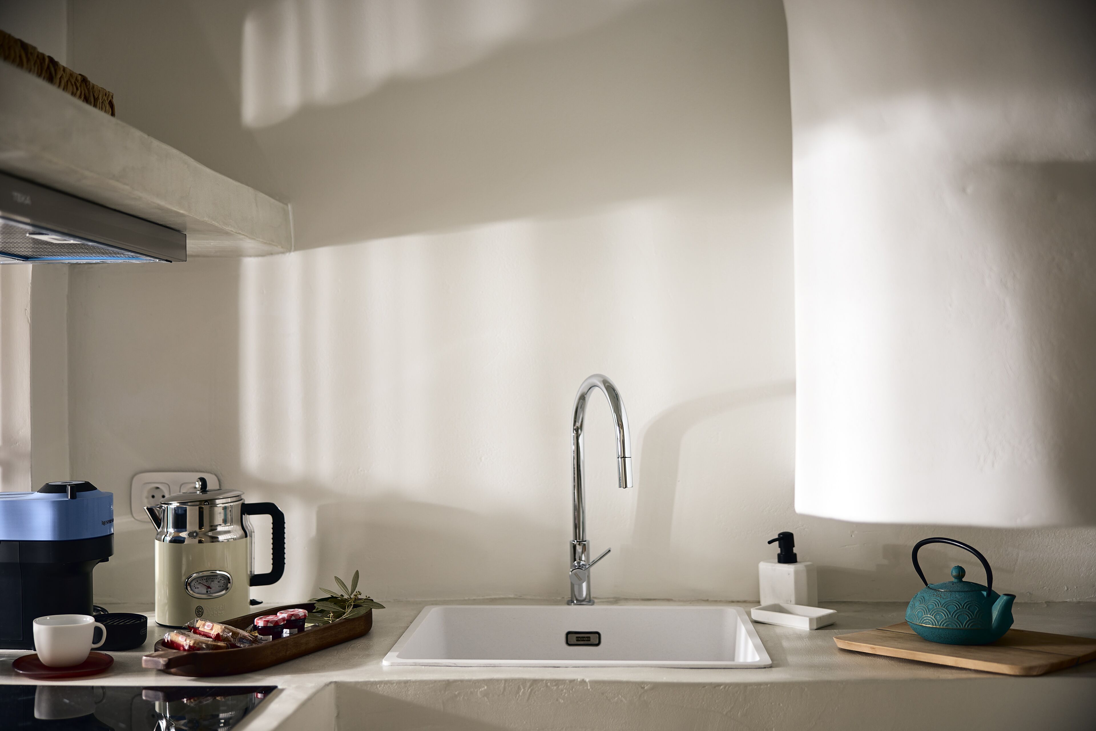 A modern kitchen with a white sink, stainless steel faucet, and a coffee maker.