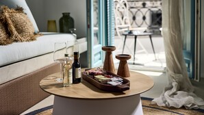 A cozy room with a bed, a round table with a tray of snacks and drinks, and a view of a balcony with outdoor furniture. - Syroc Maison (Syros)