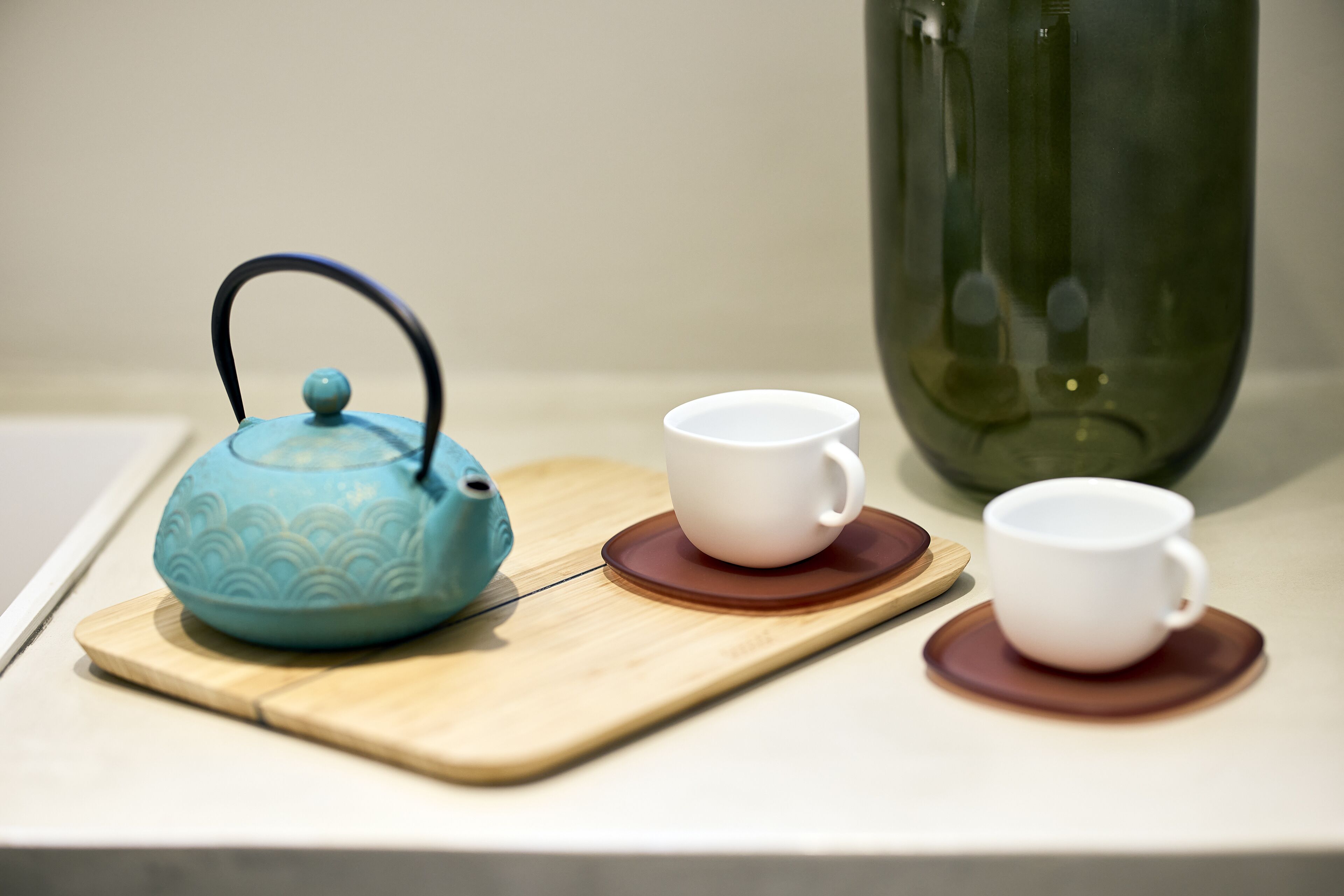 Een theeservies op een houten dienblad, met een blauwe waterkoker en twee witte kopjes op bruine schoteltjes.